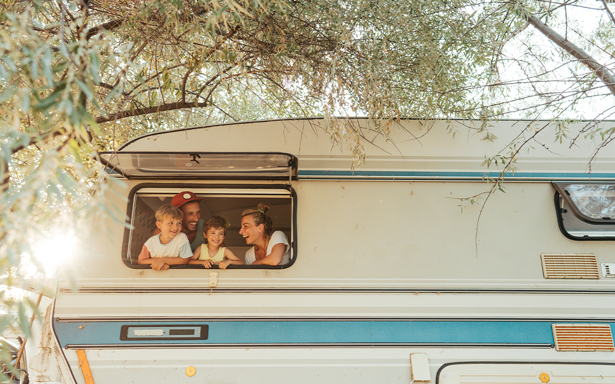Eine vierköpfige Familie, die lachend aus dem Fenster ihres Wohnwagens schaut.