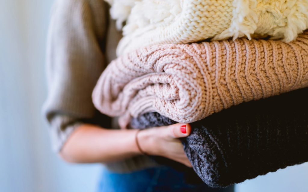 Eine Frau trägt einen Stapel frisch gewaschene Pullover