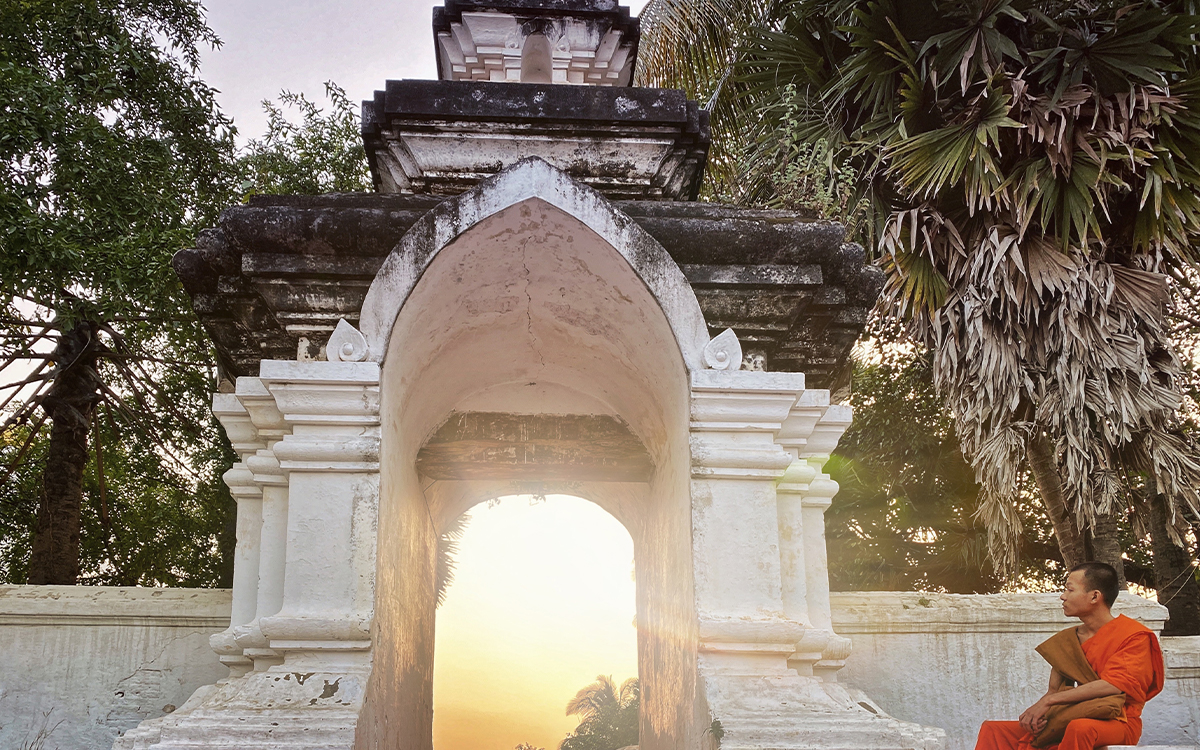 Laotischer M&ouml;nch sitzt bei Sonnenuntergang am Eingang des Tempels Wat Aham in Luang Prabang, Laos