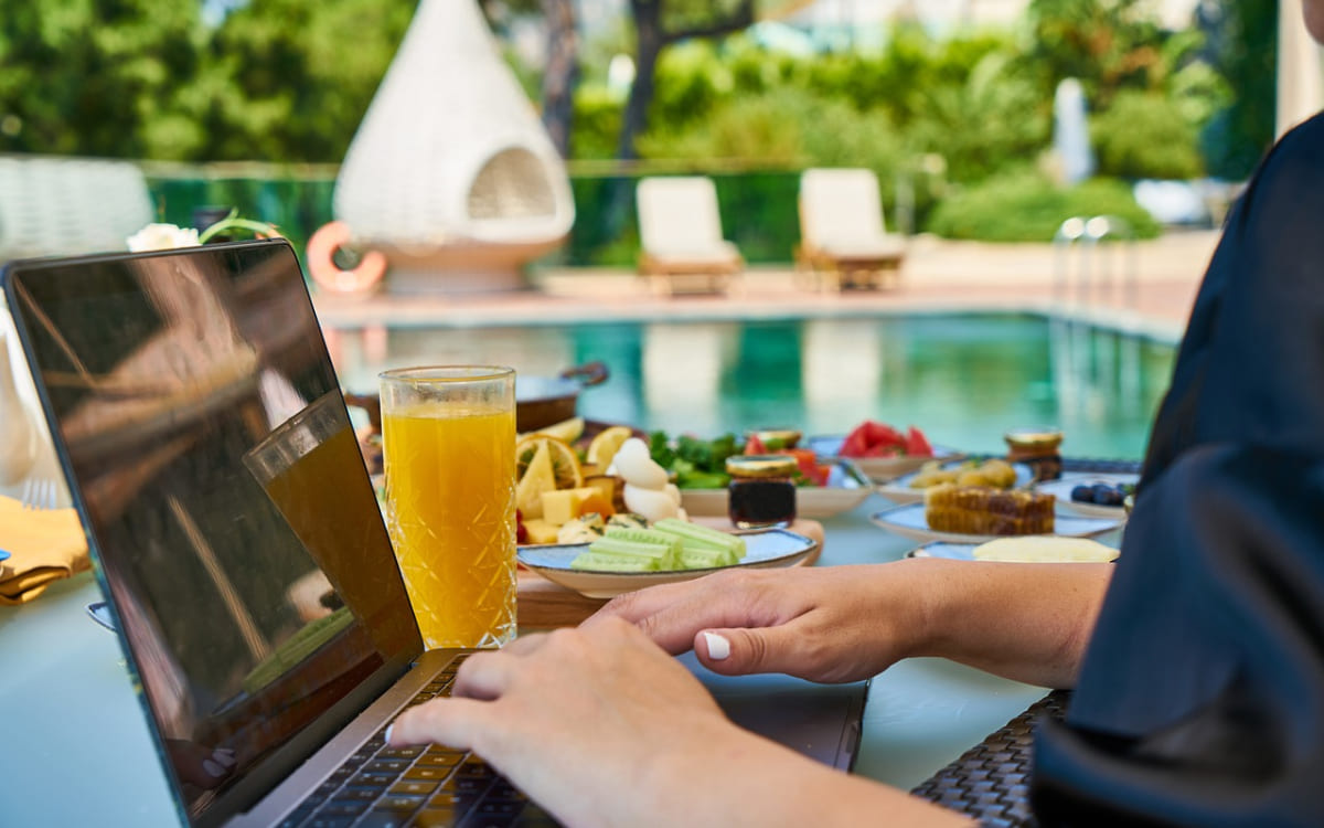 Eine Person sitzt mit Laptop am Pool, daneben steht ein ausgewogenes Frühstück.